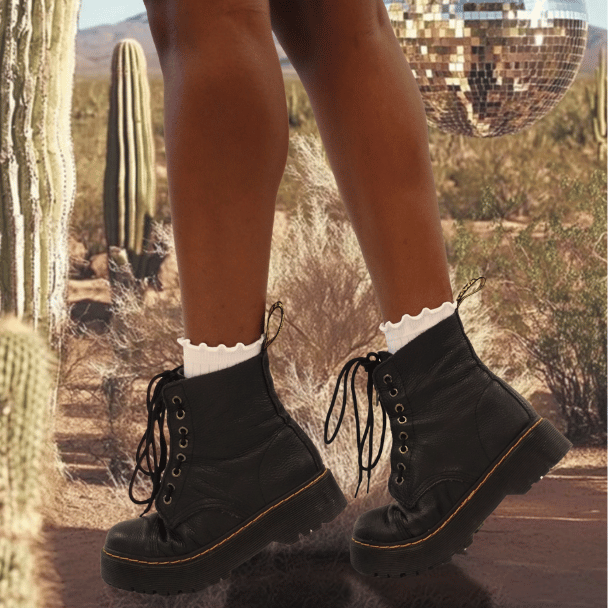Black boots with white socks worn in a desert setting with cacti and a disco ball.