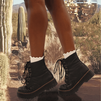 Black boots with white socks worn in a desert setting with cacti and a disco ball.