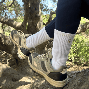 Person wearing hiking shoes and white socks standing on a rock with a natural background